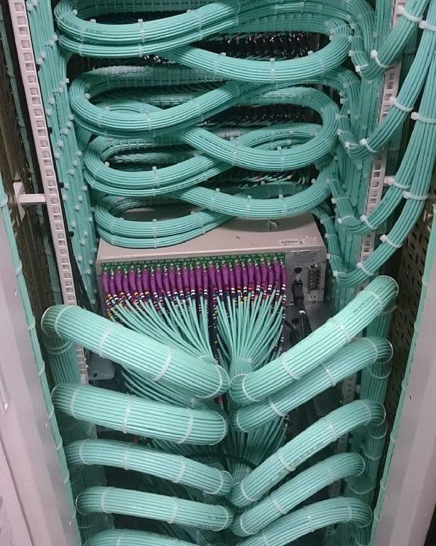 Aqua fiber cables woven through a high-density rack