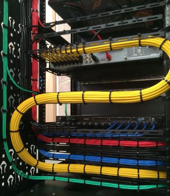 Yellow CAT6 bundle routed in a broad loop above color-coded red, blue and green rack cabling