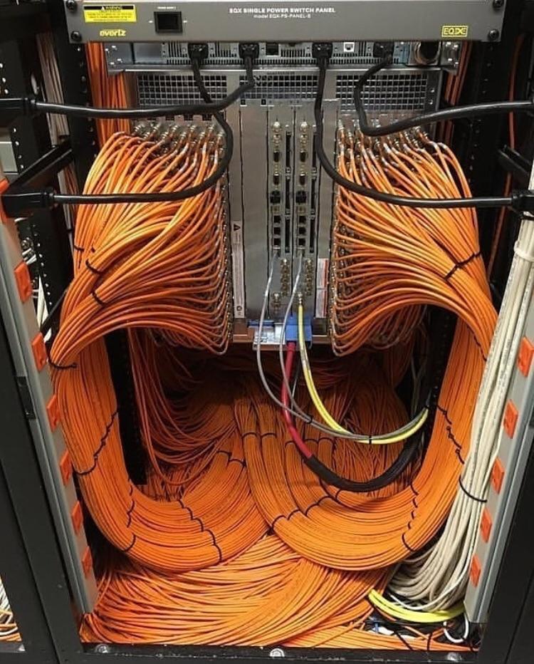 Orange network cables arranged in sweeping high-density loops inside an equipment rack